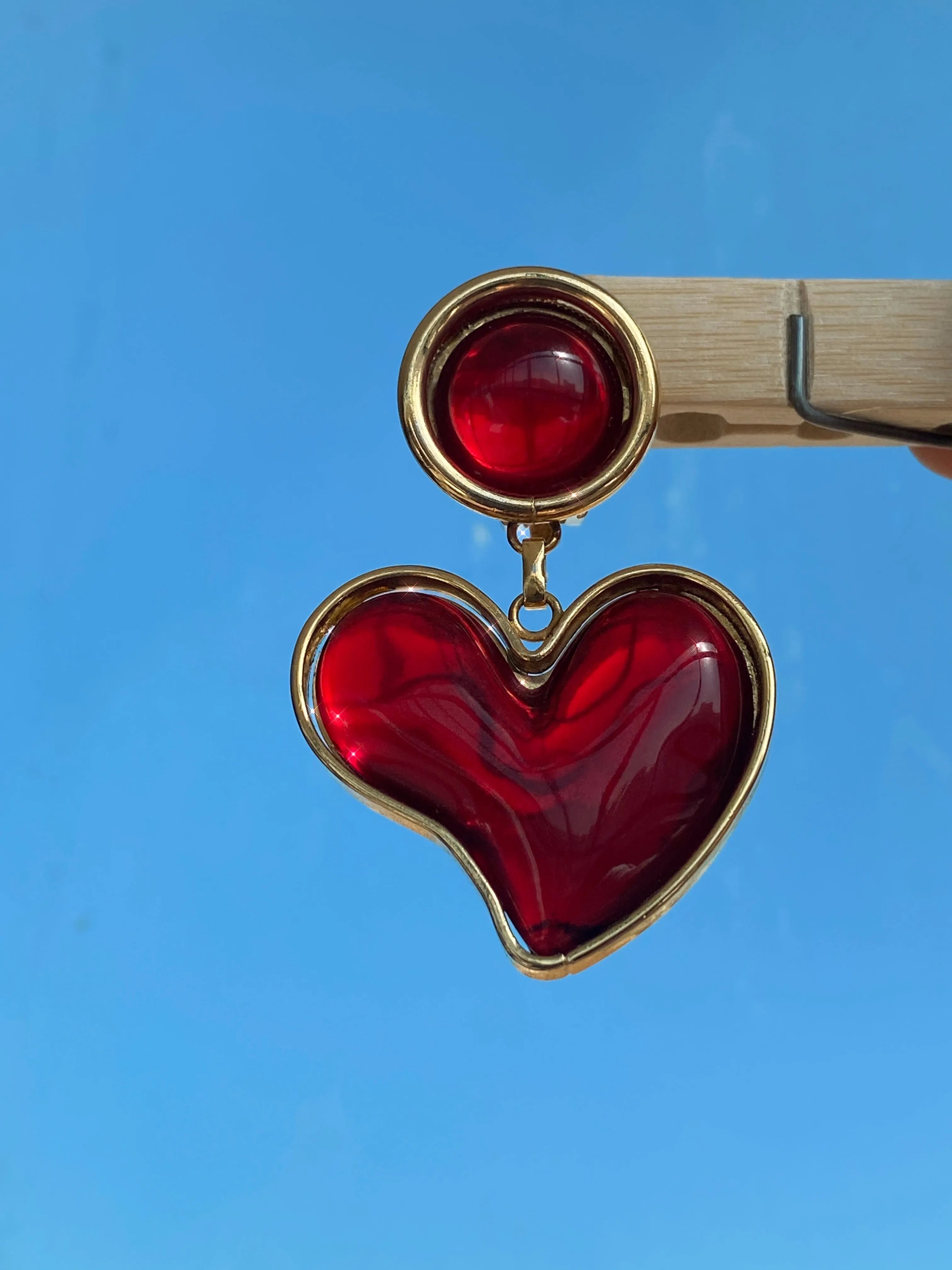Red heart-shaped vintage earring with gold trim, 90s Y2K style accessory against blue sky