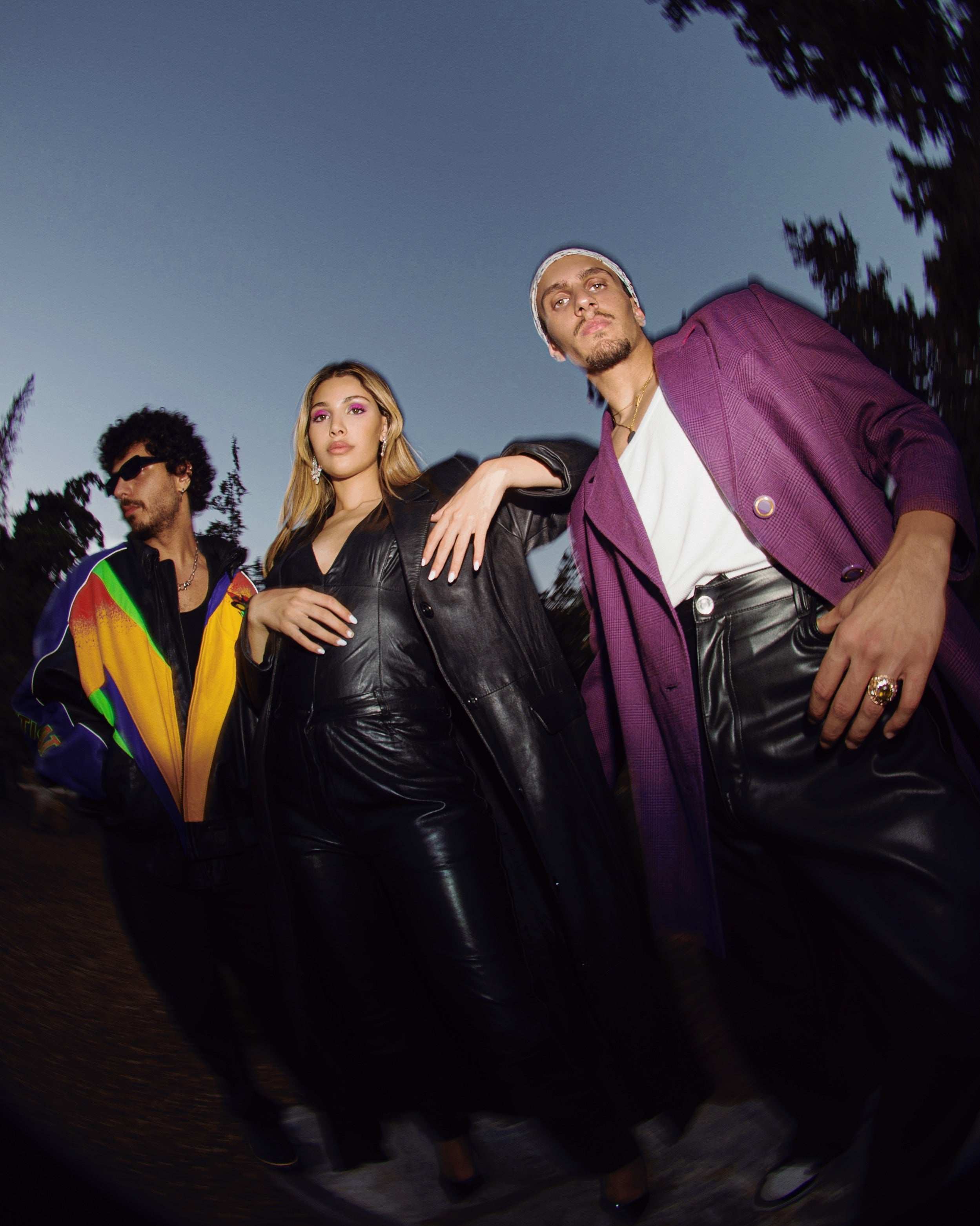 Three stylish models wearing vintage-inspired leather and colorful outerwear posing outdoors at dusk