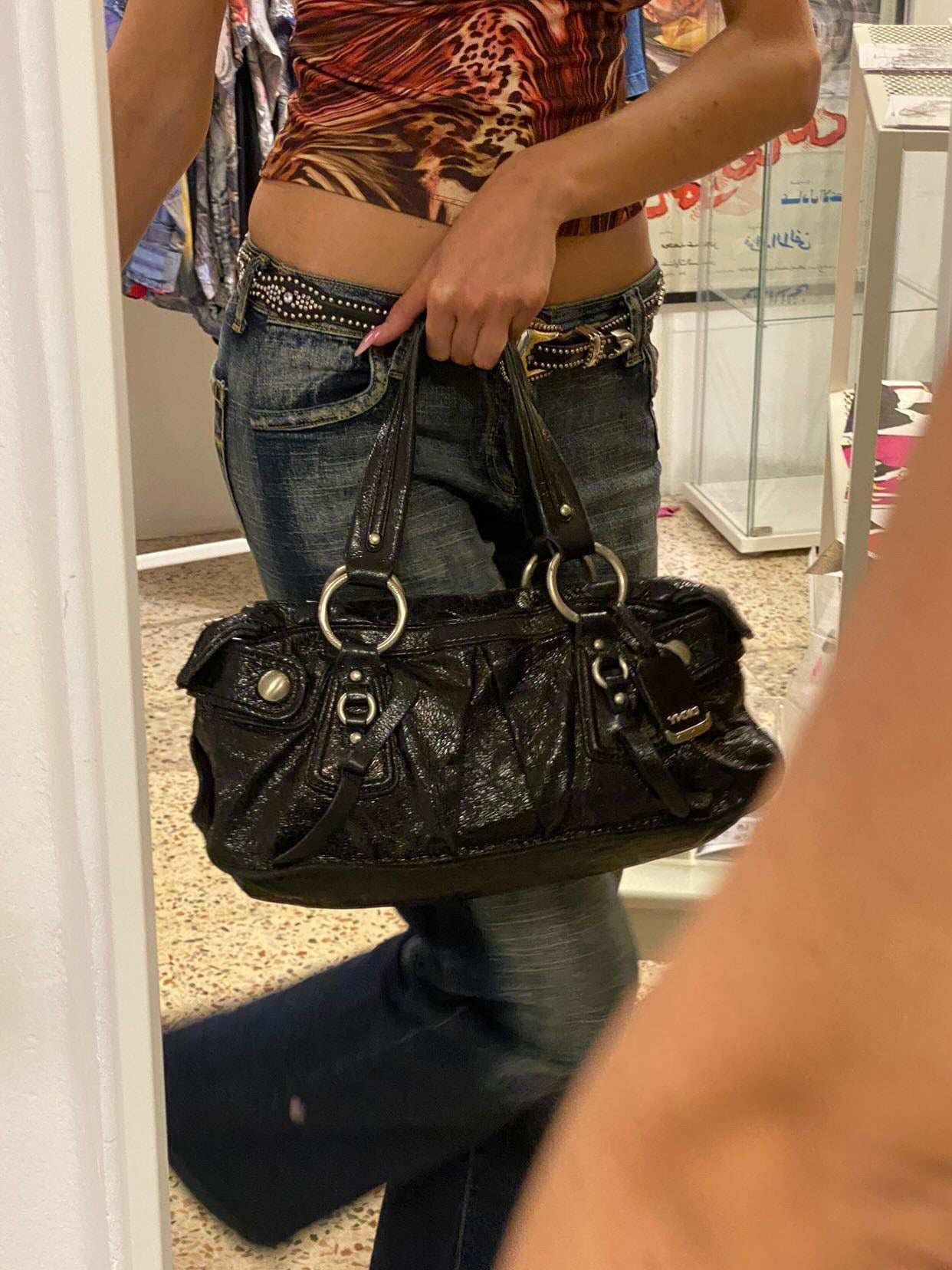 Woman holding black vintage handbag, wearing flared jeans and animal print top at Balagan Vintage shop