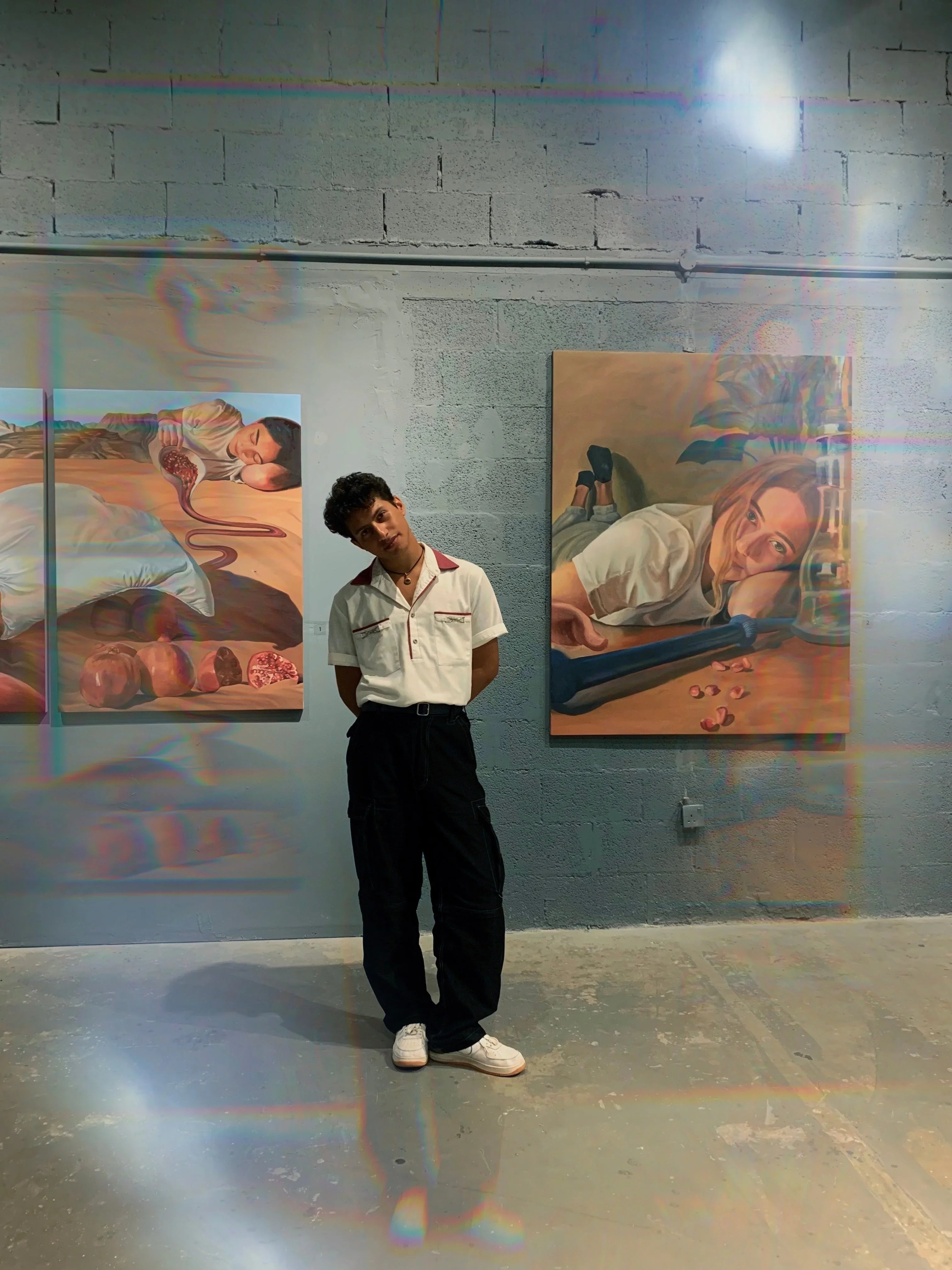 Man in vintage-style white shirt and black cargo pants posing in art gallery with surreal paintings