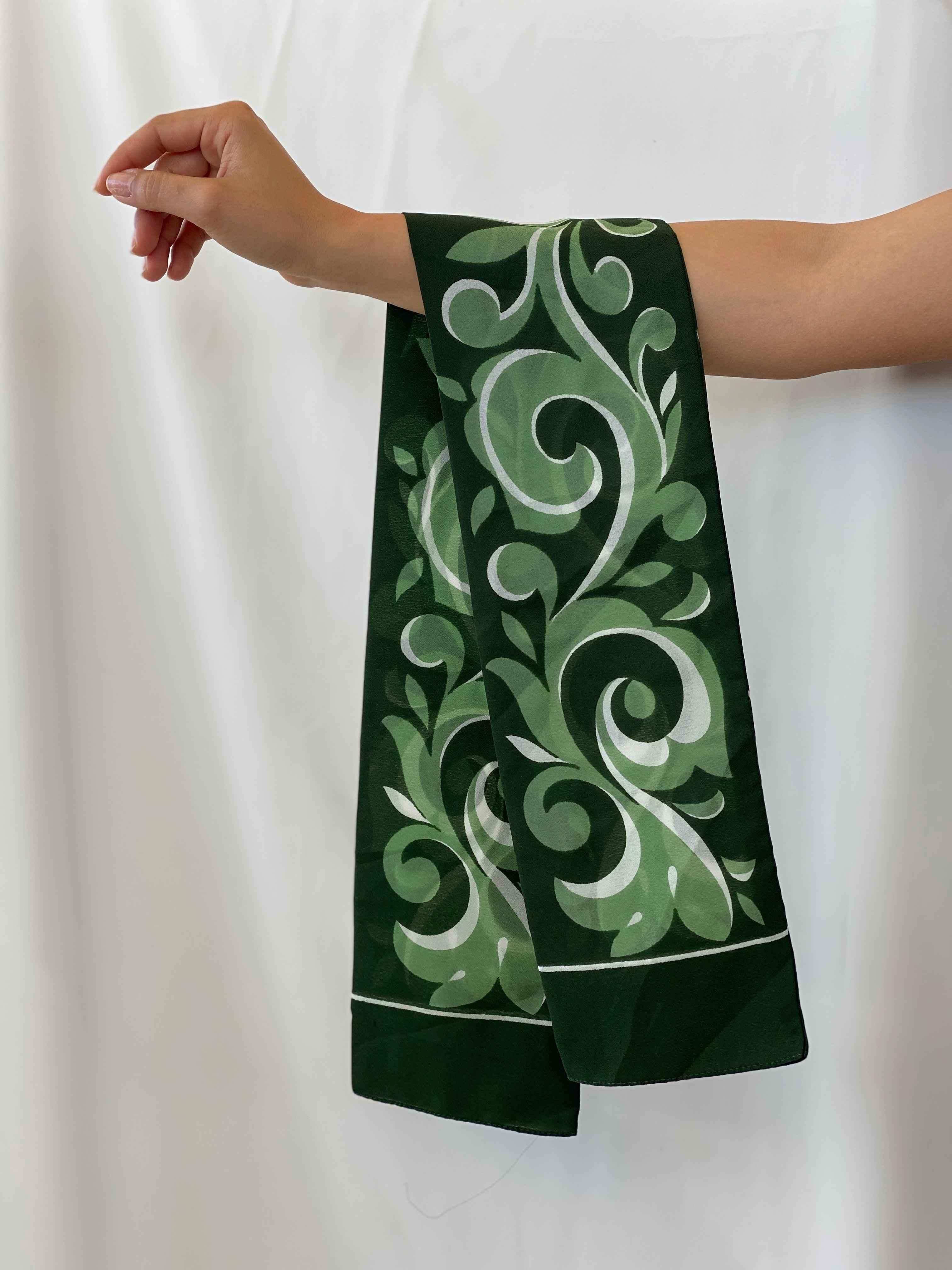 Hand holding a dark green vintage scarf with light green and white floral swirl patterns