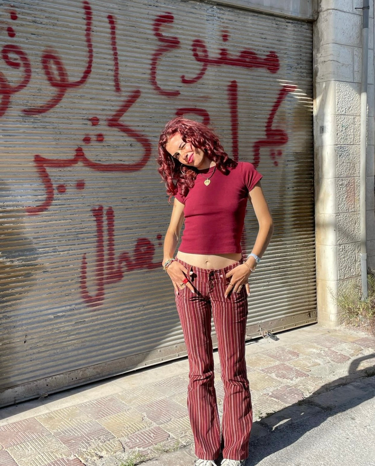 Woman in red crop top and striped vintage pants, 90s Y2K street style against graffiti shutter